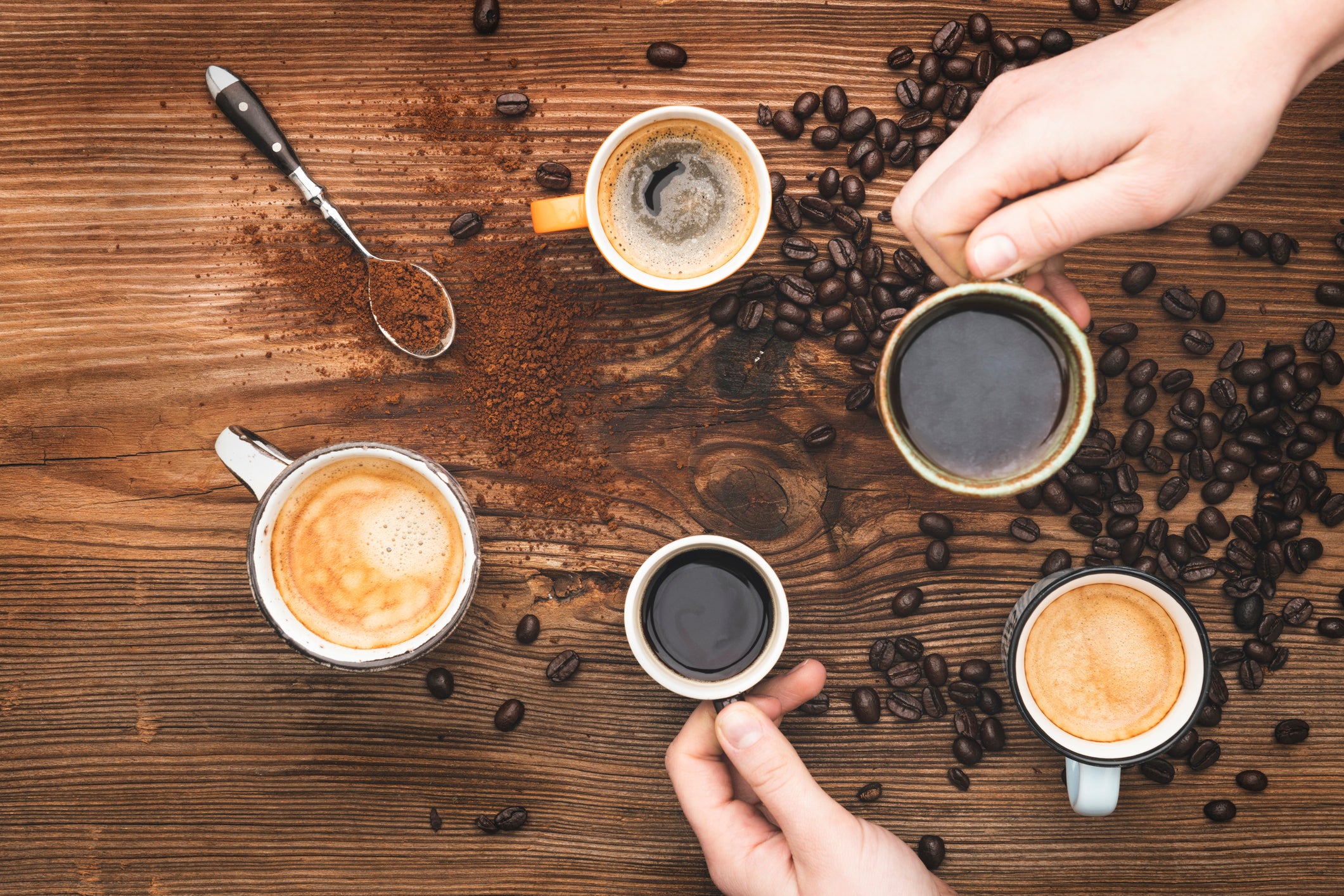 Hands grabbing cup of coffee - made by the Italia Cafe Coffee Machine on wood table covered with ground and coffee beans